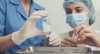 Healthcare professionals in protective gear preparing medical injection in sterile clinical environment for patient treatment and care.