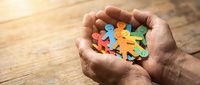 Hands holding colorful wooden puzzle pieces representing teamwork, unity and collaboration concepts for business and community projects.