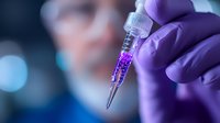 Purple gloved hand holding medical syringe with bright violet liquid against blurred laboratory background, demonstrating scientific research and medical testing concept.