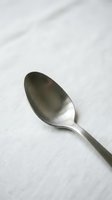 Single stainless steel spoon with brushed finish on white textured background, isolated tableware for dining, kitchen, and restaurant design use.