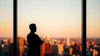 Professional businessman silhouette standing by office window overlooking city skyline at sunset, contemplating business decisions and urban development.