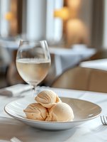Creamy peach-colored ice cream scoops served on white porcelain plate at elegant restaurant table with wine glass and soft ambient lighting in background.