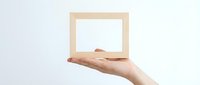 Hand holding wooden picture frame with blank white space for customization on neutral background for creative design projects.