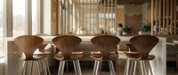 Modern wooden chairs with curved backs arranged at dining table in bright, minimalist interior space with natural light and contemporary home decor.