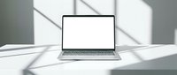 Modern laptop computer with blank white screen on minimalist desk with dramatic window shadow patterns for mockup presentations and digital workspace concepts.