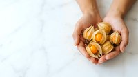 Male hands holding golden physalis fruits with papery husks on white marble surface for food styling and culinary content.