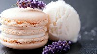 Delicate peach macarons with vanilla ice cream scoop and fresh lavender sprigs on dark slate background for gourmet dessert and bakery concepts.