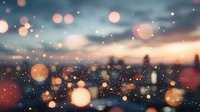 Dreamy urban skyline silhouette at dusk with soft glowing bokeh lights and particles creating magical atmospheric mood. Defocused city background.