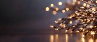 Golden lights and glowing bokeh on bare winter branches create magical holiday atmosphere against dark background with reflection on surface.