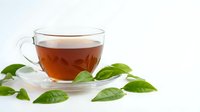 Clear glass teacup with amber herbal tea on white saucer surrounded by fresh green leaves on clean white background for wellness and natural health concepts.