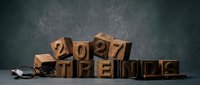 Wooden letterpress blocks spelling 2027 Trends on dark background with glasses, symbolizing future business forecasting and planning.