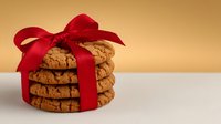 Stack of homemade chocolate chip cookies tied with elegant red ribbon bow against warm golden background, perfect for holiday gift giving or dessert promotion.