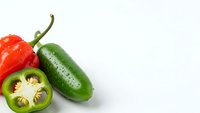 Fresh red and green jalapeno peppers with sliced cross-section showing seeds and interior on white background isolated for culinary design projects.