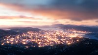Aerial panoramic view of glowing city lights nestled between mountains at dusk, with dramatic pink and purple sunset sky illuminating urban landscape.