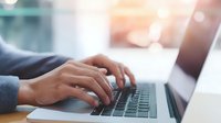 Close-up of professional hands typing on laptop keyboard in bright office environment with soft natural light, ideal for business communications.