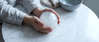 Woman hands gently holding white ceramic bowl on marble table surface in minimalist kitchen setting for mindful living and wellness concepts.