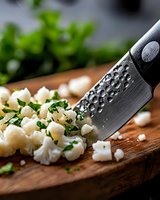 Fresh feta cheese cubes with chopped herbs on wooden cutting board, professional chef knife with water drops, close-up food photography.