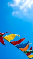 Colorful prayer flags flutter against bright blue sky with white clouds, traditional Tibetan Buddhist fabric banners used for spiritual blessings and positive energy in outdoor celebrations and religious ceremonies.