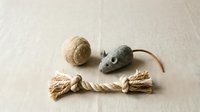 Natural cat toys set with sisal rope, felt mouse and wool ball on neutral fabric background for pet care and feline entertainment.