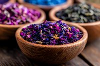 Aromatic dried flower petals and herbs in wooden bowl on rustic table, purple and blue botanical mix for tea, aromatherapy, and natural wellness products.