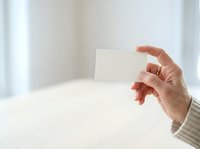 Mature woman with light skin tone holding blank white card in hand against bright neutral background, suitable for business, marketing, and promotional materials.