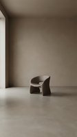 Minimalist sculptural armchair in neutral tones positioned in empty gallery space with concrete flooring and beige walls, suitable for interior design and contemporary furniture concepts.