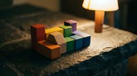 Colorful wooden building blocks arranged on textured surface with warm lamp lighting creating cozy educational play environment for children development.