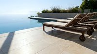 Luxury infinity pool terrace with wooden sun loungers overlooking ocean view, modern resort architecture and tropical landscaping for vacation relaxation.