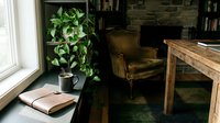 Cozy home office corner with wooden desk, leather armchair, potted plant, and open book on floor near window with natural light.