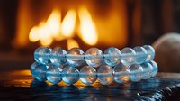 Luminous blue crystal bracelet with transparent beads glowing in warm firelight against dark background, creating magical atmosphere and spiritual ambiance.