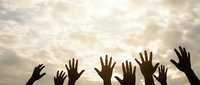 Silhouettes of diverse hands raised up against dramatic cloudy sky at sunset, symbolizing unity, hope, volunteering and community support concepts.