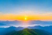 Majestic sunrise over misty mountain ranges with vibrant orange and blue sky, layers of rolling hills covered in morning fog creating peaceful natural landscape.