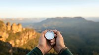 Hands holding compass with mountain landscape view at sunrise, navigation and travel concept for outdoor adventure and exploration.