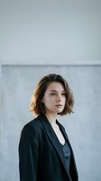 Professional young Caucasian businesswoman with short brown hair in black blazer standing confidently in modern office interior for corporate branding.