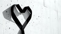 Black ribbon heart shape casting shadow on white textured wall with scattered dark spots creating romantic minimalist composition for love concepts.