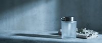 White ceramic mug with silver handle on concrete surface against textured gray wall. Minimalist kitchen scene with natural lighting and shadows.