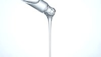Transparent liquid pouring from tilted bottle against white background, suitable for beverage, skincare, or pharmaceutical product marketing and packaging design.