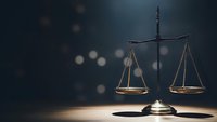 Scales of justice on wooden surface with dramatic lighting and bokeh background for legal concepts and law firm presentations.