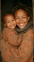 African American mother and daughter sharing joyful moment in warm knit sweaters. Close-up portrait showing genuine happiness and family connection in natural lighting.