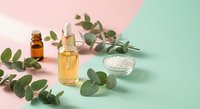 Natural eucalyptus essential oil bottles with fresh green leaves and sea salt on pastel pink and mint background for aromatherapy wellness spa treatments.