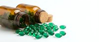 Green capsules spilling from amber glass bottle on white background. Medical supplements, vitamins, pills scattered for healthcare and pharmaceutical concepts.
