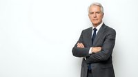 Confident mature Caucasian businessman in dark suit with crossed arms standing against white background, professional corporate executive portrait.