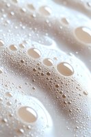 Water droplets and bubbles on white surface create abstract macro pattern with soft beige tones, showing surface tension and condensation effects.
