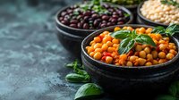 Fresh chickpeas and red kidney beans in black ceramic bowls garnished with basil leaves on dark textured background. Mediterranean cuisine ingredients.
