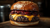 Juicy beef burger with melted cheddar cheese, crispy bacon strips, and sesame seed bun photographed in dark moody setting with dramatic lighting.