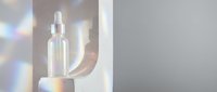 Clear glass spray bottle with liquid serum or essential oil on white podium with soft light refraction and bokeh background for skincare and cosmetic product marketing.