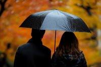 Romantic couple sharing black umbrella against vibrant autumn foliage background, silhouetted figures in rain create atmospheric mood for seasonal photography.