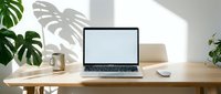 Laptop with blank white screen on wooden desk in bright minimal home office with monstera plant and coffee mug, mockup for design.