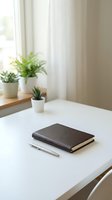 Minimalist workspace with leather notebook and pen on white desk near window with small potted plants creating calm productive atmosphere for writing.
