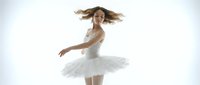 Young female ballet dancer with long brown hair, wearing white tutu and pointe shoes, performing graceful spin with hair in motion against white background for dance, performance, and arts content.
